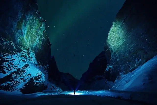 Lone hiker with headlamp standing in narrow ice canyon under starry night sky in Stakkholtsgja Canyon, Iceland