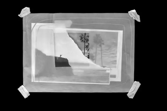 Black and white travel photograph taped to a dark surface showing a white architectural structure with palm trees, demonstrating the concept of transforming travel photos into physical art displays
