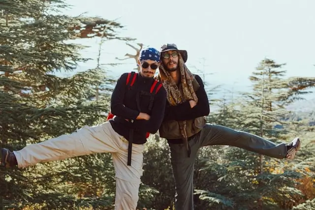 Two adventurous friends posing playfully on a mountain trail surrounded by tall cedar trees during their hiking trip