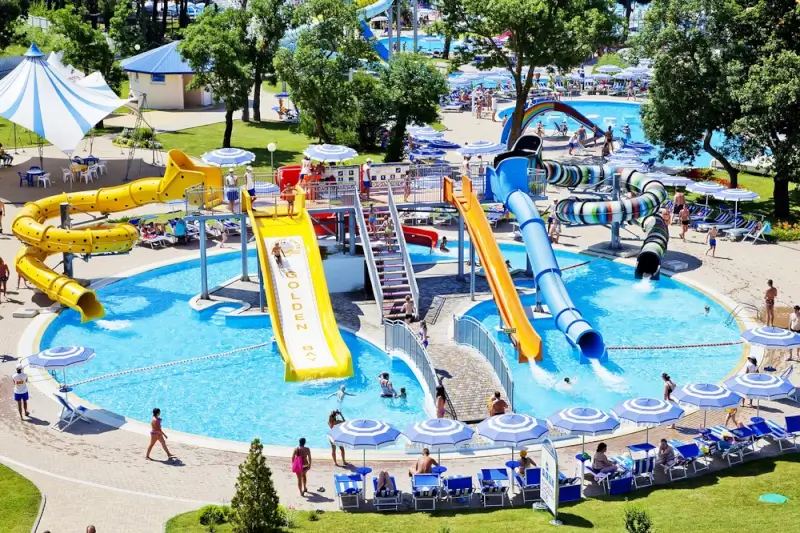 Aerial view of outdoor Swiss water park with multiple colorful slides, pools, and families enjoying summer day