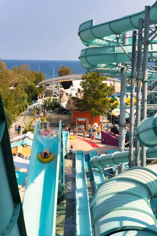 Water park slides with lake or sea view, showing visitors on tubes descending blue slides at outdoor Swiss aquatic facility