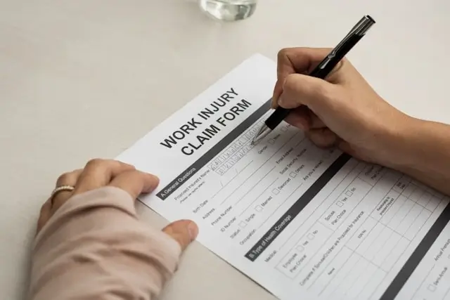 Close-up of a person filling out a work injury claim form with a pen on a desk.
