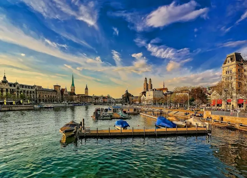 Zurich cityscape with historic church spires along Limmat River waterfront and boats at sunset, Switzerland