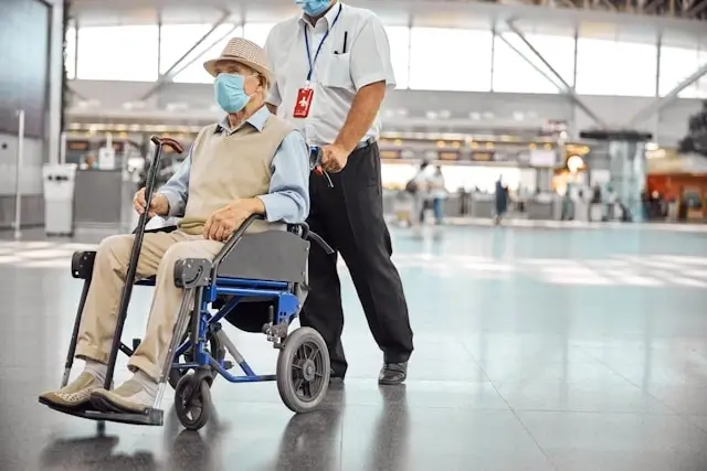 Airport staff providing VIP assistance to elderly passenger with reduced mobility in wheelchair