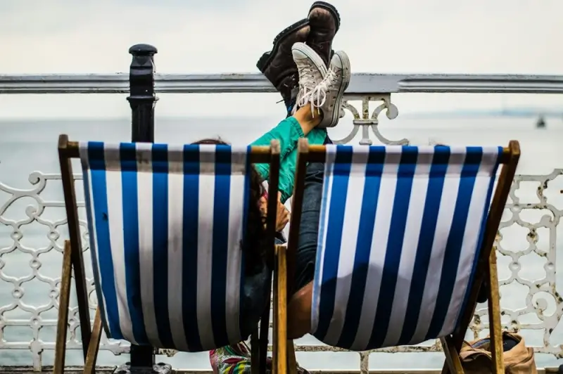 Couple relaxing on striped deckchairs by the sea in Brighton coastal town UK