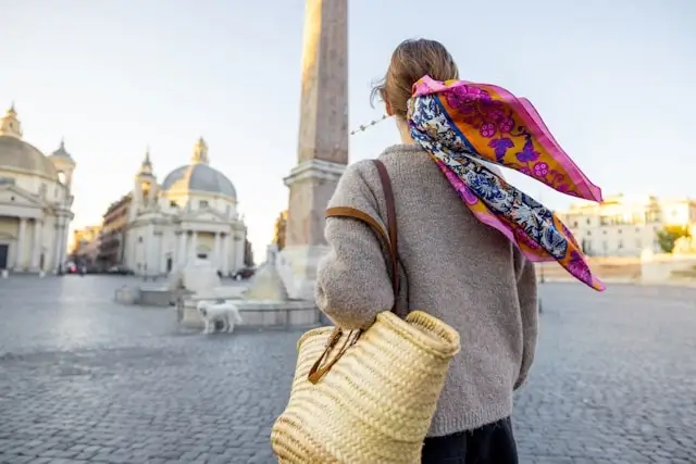 Woman with colorful scarf and woven bag exploring Piazza del Popolo in Rome during golden hour, embodying slow travel for women in Italy