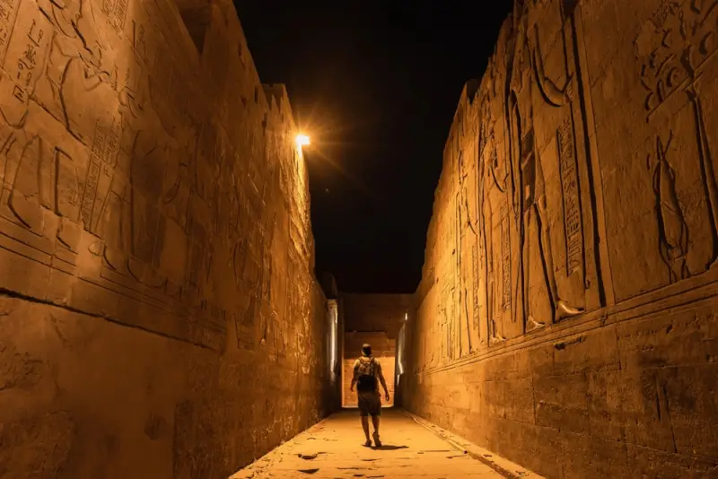 Tourist walking through ancient Egyptian temple corridor with hieroglyphic walls in Aswan, a prime location for August 2027 eclipse viewing