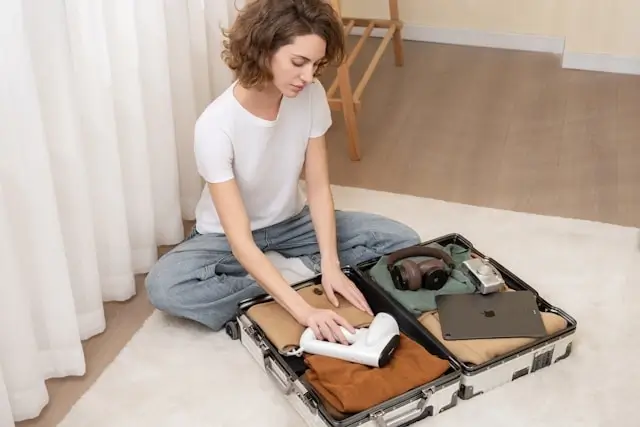 Woman sitting on floor mindfully packing minimalist suitcase with folded clothes and essentials for intentional travel