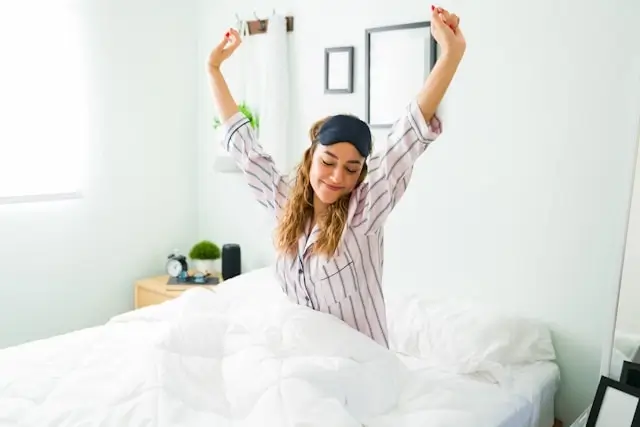 Woman stretching happily in comfortable striped pajamas after learning how to sleep well in unfamiliar hotel bedroom