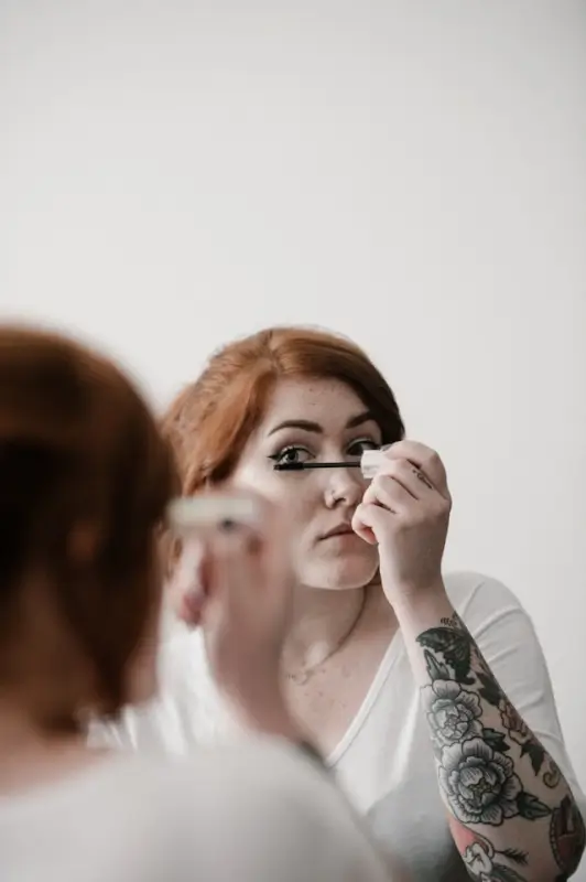 Woman applying mascara in mirror during morning beauty routine, maintaining self-care rituals while traveling