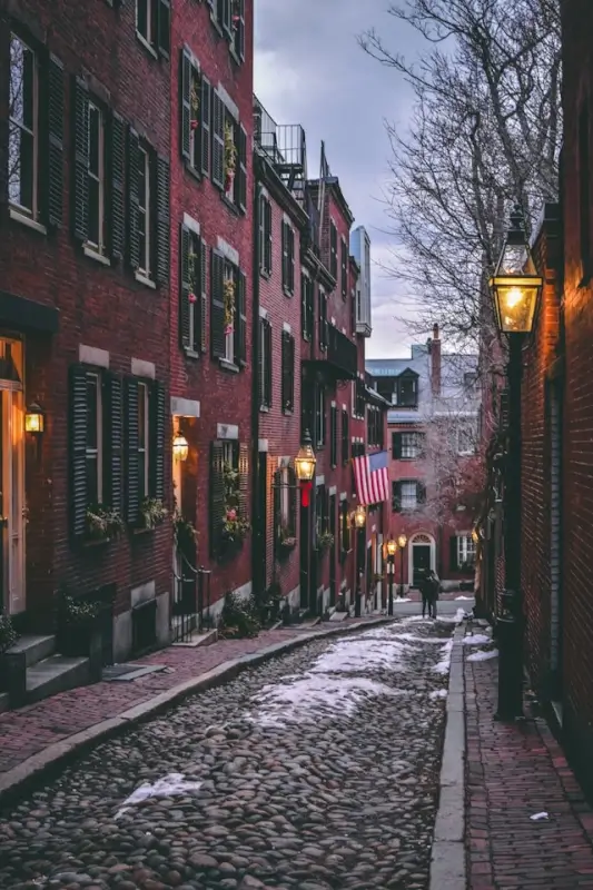 Cobblestone Acorn Street lined with historic brick rowhouses and glowing gas lamps in Boston's Beacon Hill neighborhood