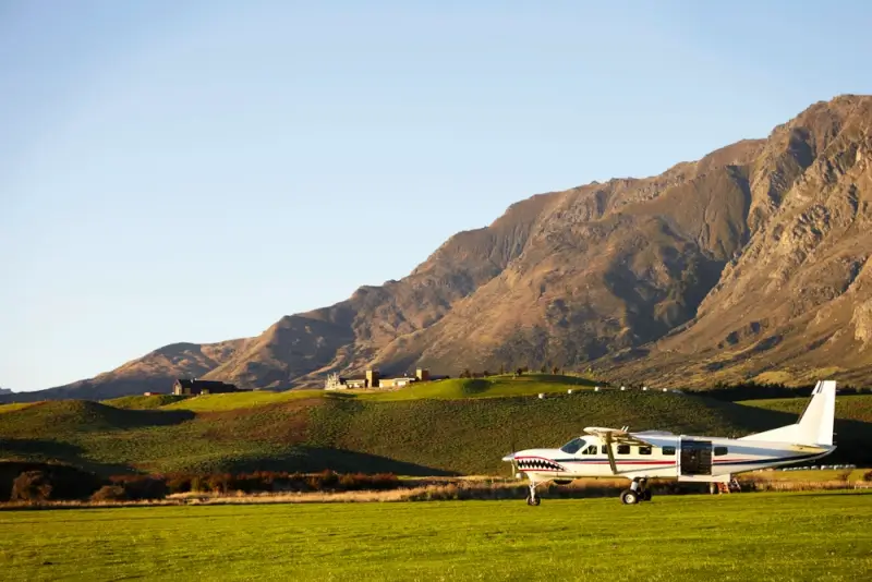 Skydiving aircraft parked on green airfield with the Remarkables mountain range in Queenstown, New Zealand