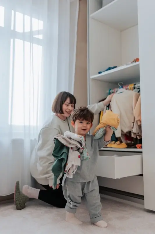 A young child helping an au pair sort clothes in a bedroom wardrobe, showing a daily family routine while hosting an au pair.