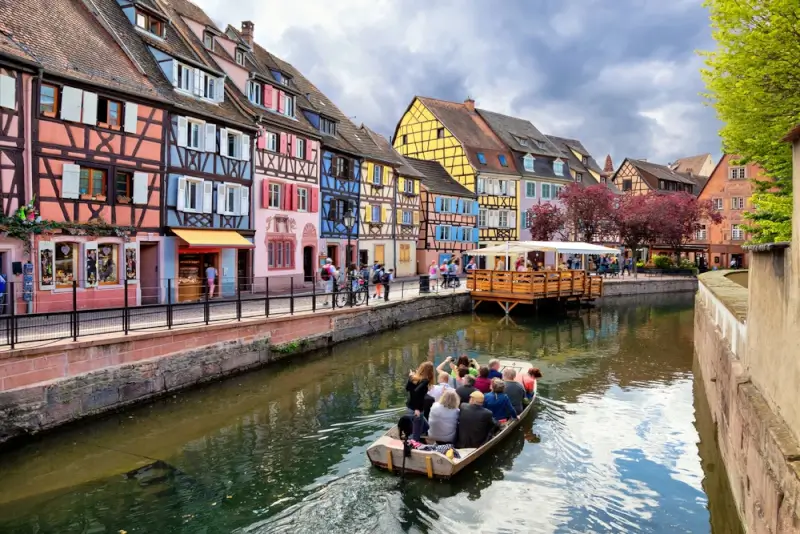 Tourists on a canal boat tour passing colorful half-timbered houses in Colmar, France