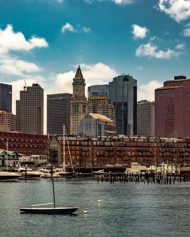 Boston Harbor waterfront with sailboats, historic Custom House Tower, and downtown skyline under blue skies