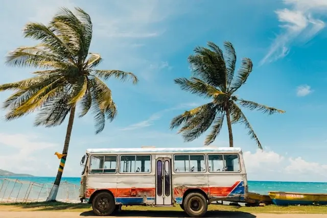 Colorful vintage bus parked between palm trees along Jamaica's coastline with turquoise Caribbean Sea in background