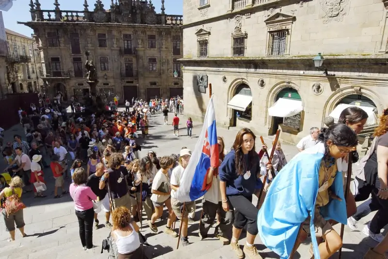 Pilgrims carrying flags gathering in historic Santiago square surrounded by traditional Spanish architecture and crowds