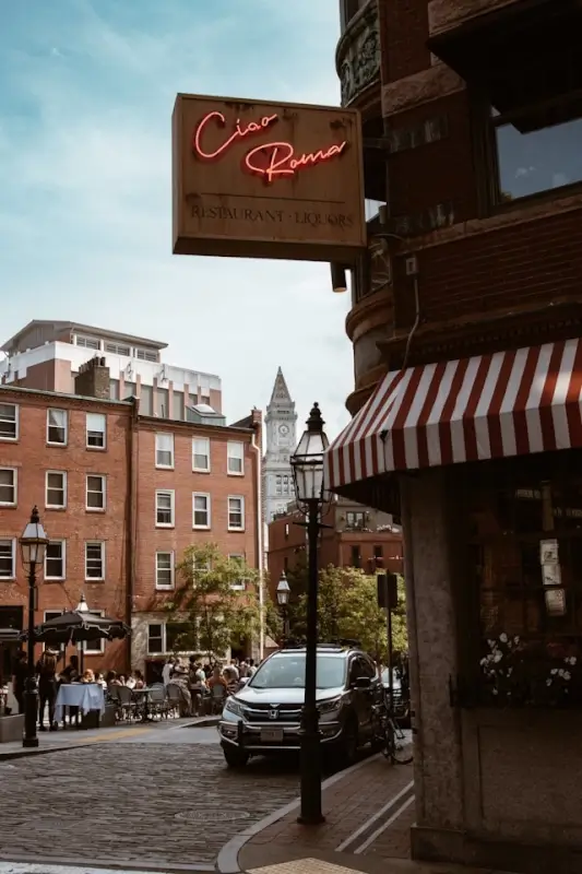 Ciao Roma Italian restaurant with neon sign and striped awning on a cobblestone street in Boston's North End