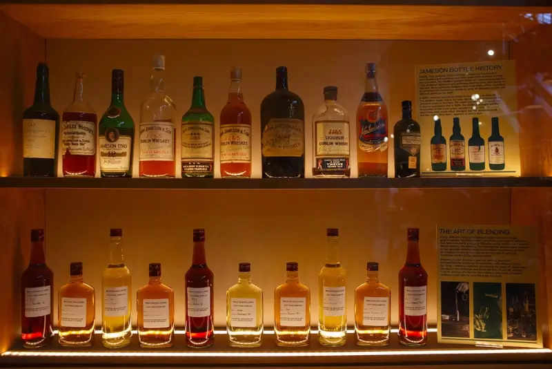 Collection of vintage and modern Irish whiskey bottles displayed on illuminated shelves at a distillery museum, showcasing Ireland's rich whiskey-making heritage