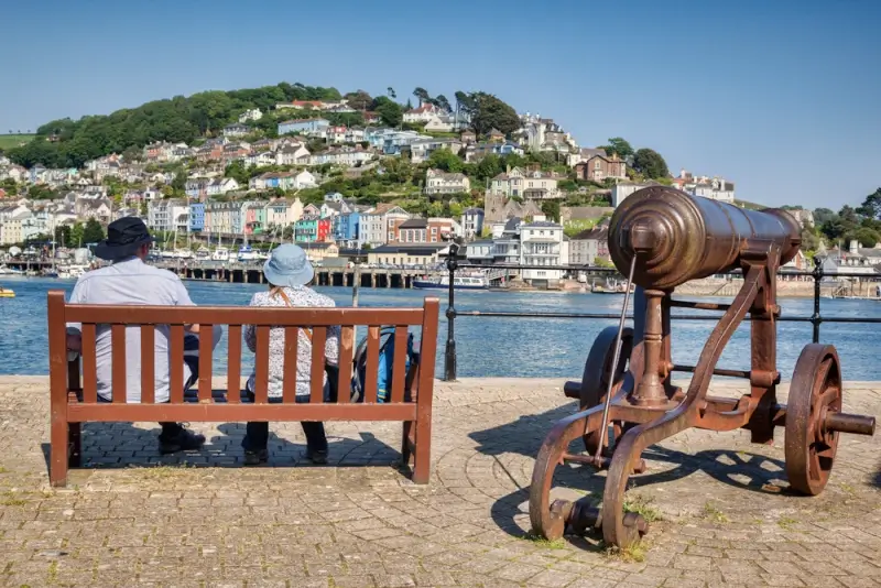 Couple on bench overlooking colorful harbor and hillside town in Dartmouth Devon