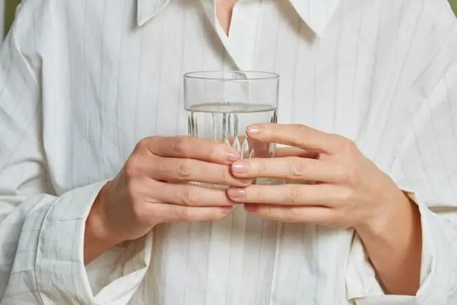 Person in white pajamas holding glass of water for proper hydration before bedtime to prevent travel-related sleep disruption
