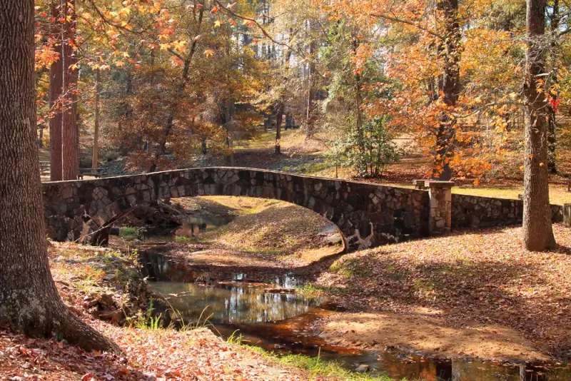Stone arch bridge over creek at Flat Rock Park in Columbus Georgia surrounded by vibrant orange and gold fall foliage