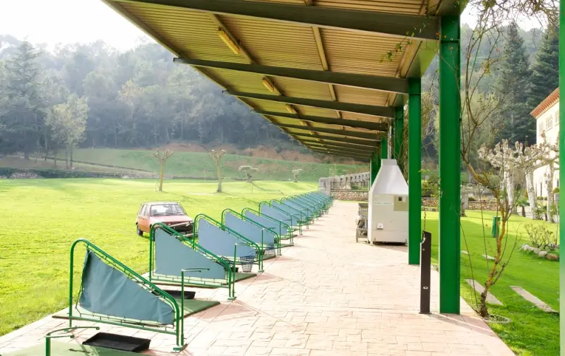 Golf driving range in Barcelona with practice bays and mountain forest backdrop