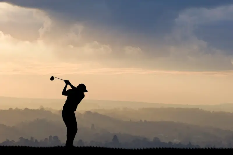 Golfer silhouette at sunset with misty countryside landscape during European golf vacation