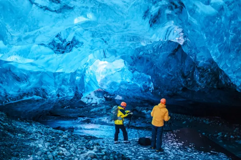 Two travelers exploring a blue ice cave under a glacier in Iceland on a guided tour