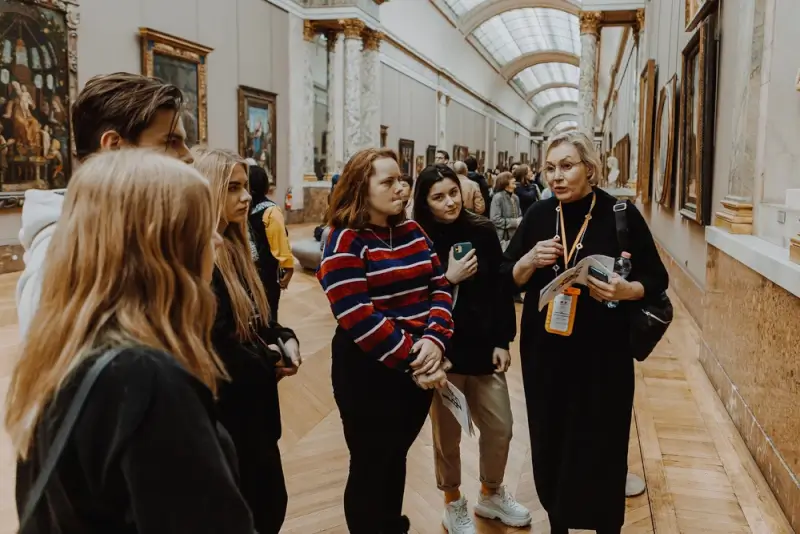Tour guide leading a group of visitors through the Louvre Museum gallery in Paris