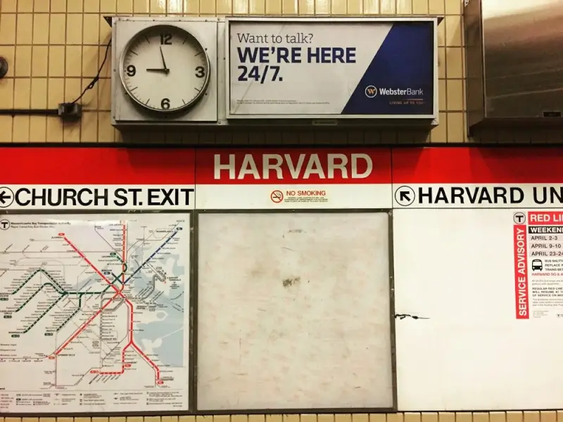Harvard University subway station platform with red line sign, transit map, and vintage clock in Cambridge, MA