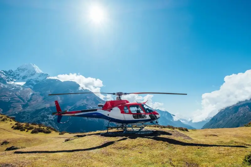 Red and white helicopter on mountain landing pad with snow-capped Himalayan peaks during Everest region tour in Nepal