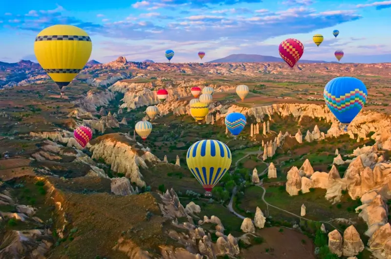 Multiple hot air balloons drifting over fairy chimneys and rock formations at sunrise in Cappadocia, Turkey