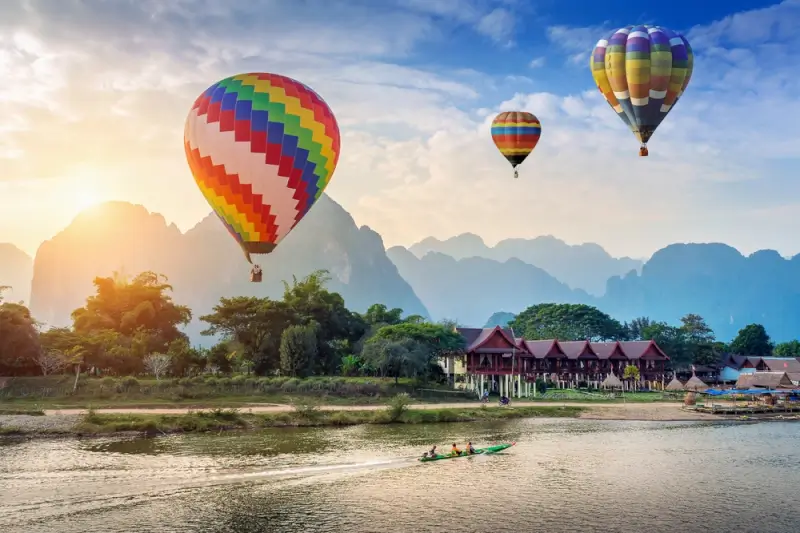 Hot air balloons floating above Nam Song River with dramatic limestone karst mountains in Vang Vieng, Laos