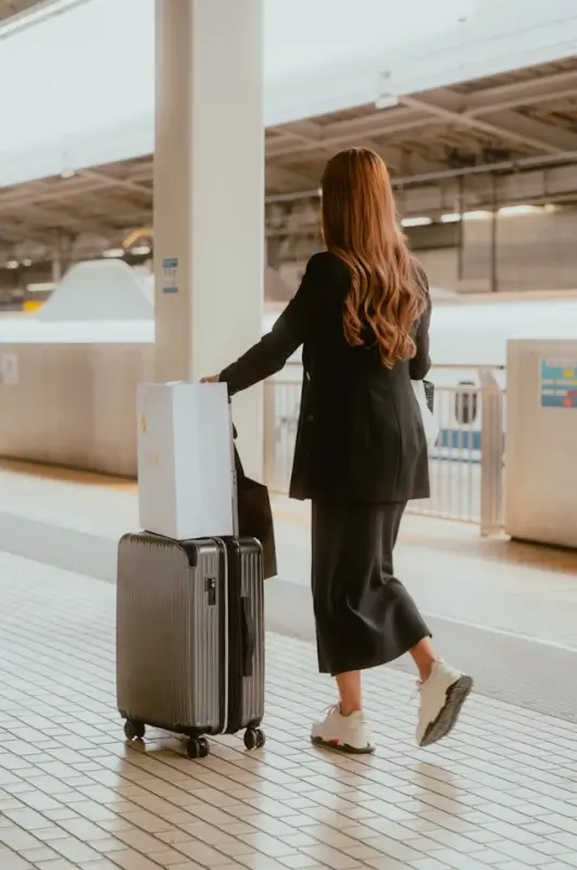 Woman with suitcase and shopping bags walking through modern train station platform