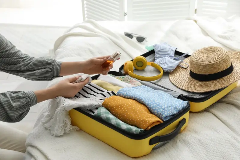 Traveler packing travel size fragrance bottles in suitcase with clothes and accessories