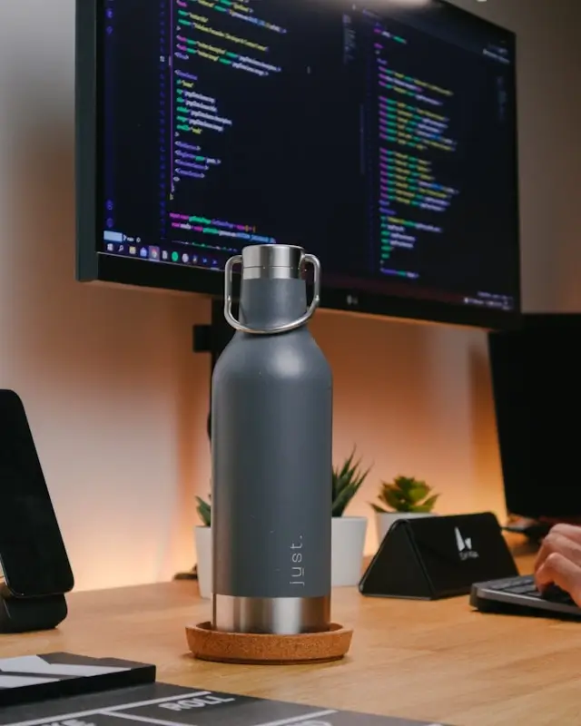 Gray minimalist insulated water bottle on desk with computer workspace and succulents