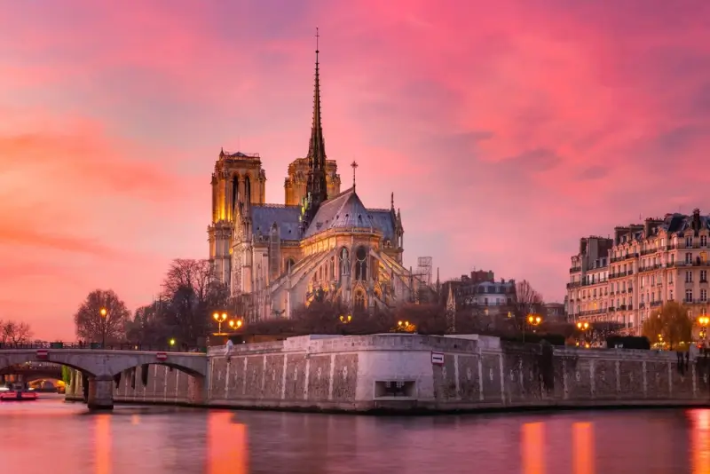 Notre Dame Cathedral illuminated at sunset with pink and orange sky over Seine River in Paris France