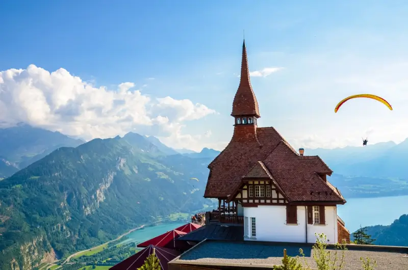 Paragliders soaring above Harder Kulm chapel with turquoise alpine lakes and Swiss mountain peaks in Interlaken