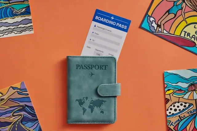Passport holder with boarding pass and travel postcards on colorful background