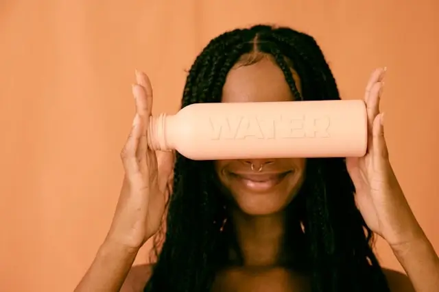 Woman holding peach-colored reusable water bottle with embossed text against orange background