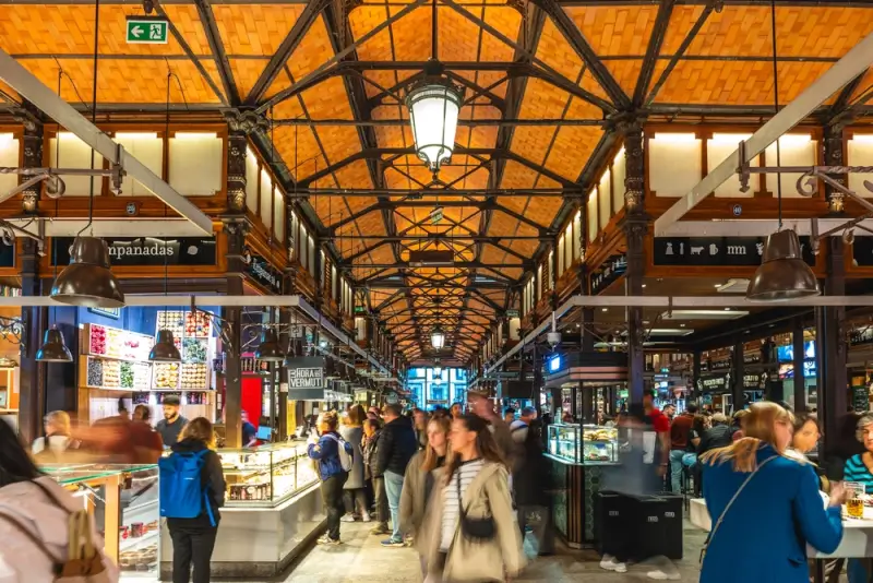 Mindful tours through San Miguel Market in Madrid Spain with crowds browsing food stalls under ornate iron and tile ceiling