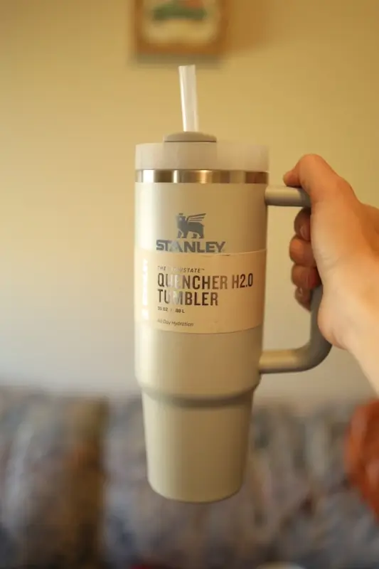 Stanley Quencher H2O tumbler in cream color with straw, held by hand showing insulated travel mug