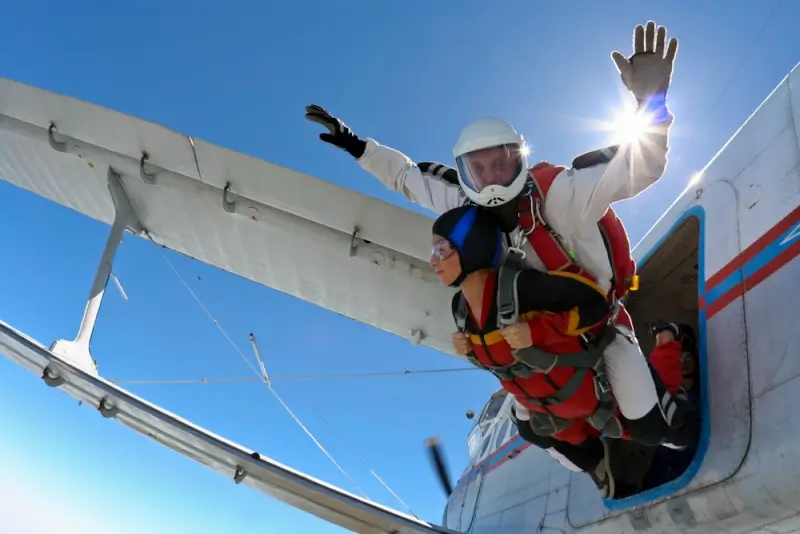Tandem skydiving jump from aircraft with instructor and student exiting plane against clear blue sky