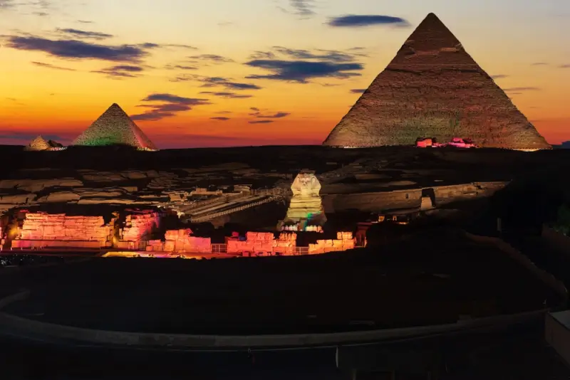 Great Pyramids of Giza and Sphinx illuminated at sunset with colorful light show, iconic Egyptian monuments under dramatic twilight sky