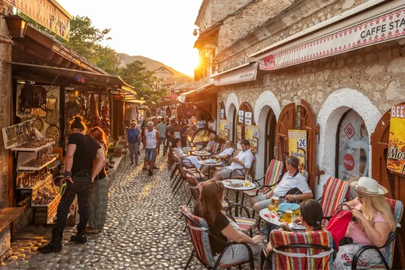 Tours for solo travel in Europe: travelers dining at outdoor cafes on a cobblestone street in Mostar Old Town, Bosnia