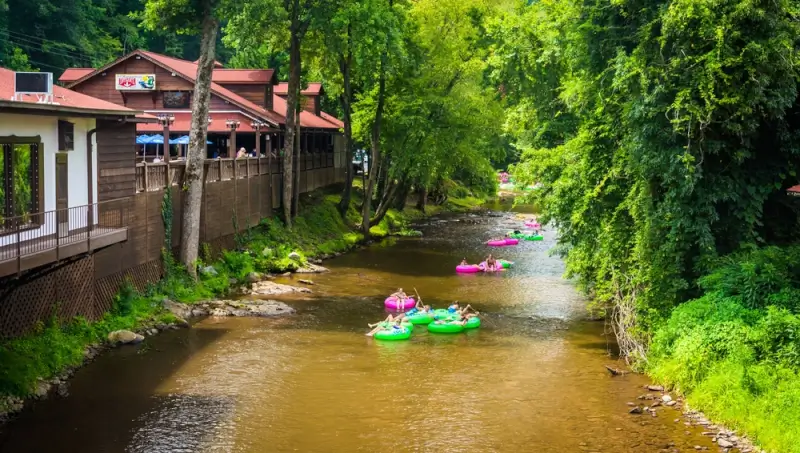 People floating on colorful tubes down the Chattahoochee River in Columbus Georgia with riverside restaurant and lush green trees