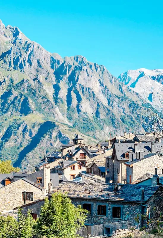 Traditional stone houses with slate roofs in mountain village beneath towering jagged peaks and bright turquoise sky