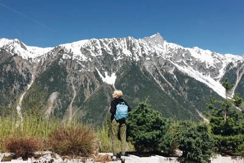 Woman with blue backpack hiking in Mont Blanc admiring panoramic views of snow-capped Alpine peaks and forested valleys