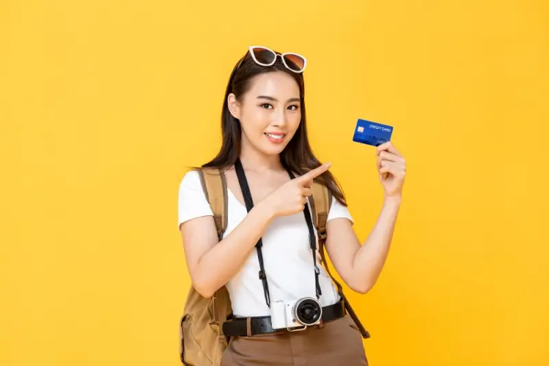 Woman traveler with camera and backpack holding credit card for travel rewards and points